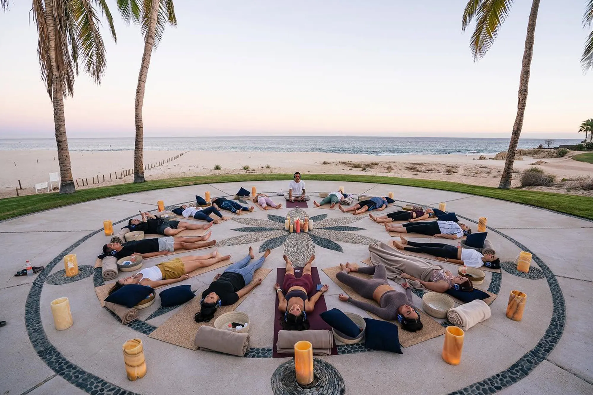 Circle of yoga mats by the sea, with candles and wireless headphones, during a guided relaxation