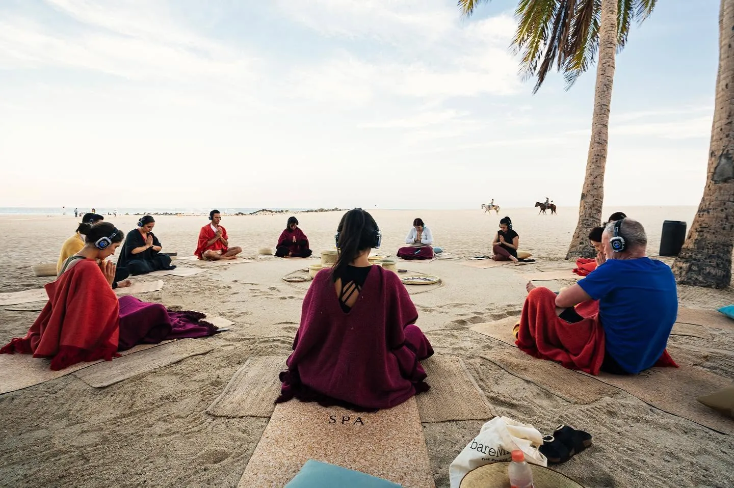Group sitting in a circle on the beach, hands together, wearing wireless headphones