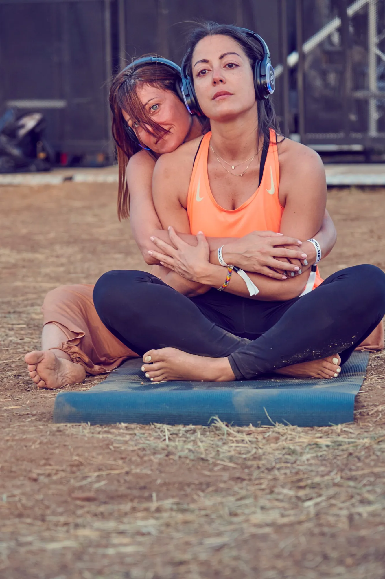 Two participants hugging on a yoga mat at a festival, wearing wireless headphones